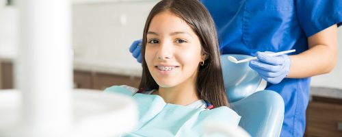 Portrait of smiling teenage girl with braces sitting on chair while dentist standing in clinic